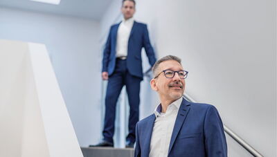 Kanzlei für Steuerberatung und Wirtschaftsprüfung Zwei Männer stehen in einem Treppenhaus, den Blick zur Seite gerichtet